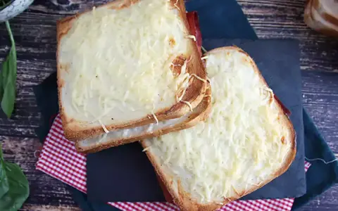 Två gyllene croque monsieur-smörgåsar med smält ost och skinka, serverade på en rutig duk.
