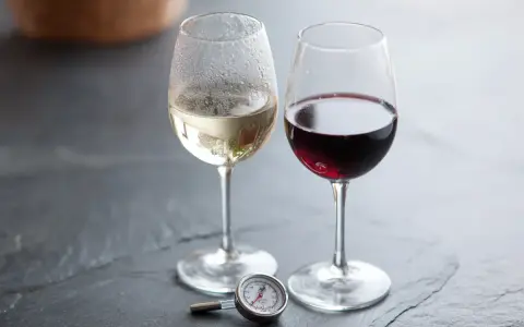 Två glas vin, ett vitt och ett rött, med en termometer bredvid. Perfekt vitt vin temperatur är viktigt för njutning.