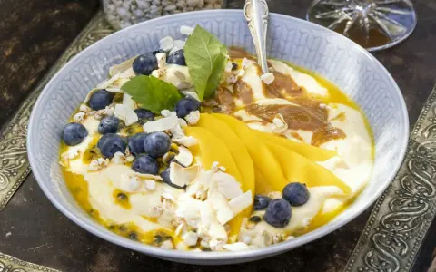 En skål med yoghurt, blåbär, passionsfrukt och vackert skivad mango. Toppad med kokoschips och puffat spannmål.