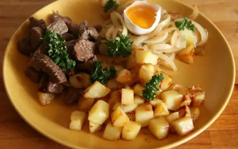 En tallrik med stekt kött, stekt potatis, stekt lök och ett kokt ägg. Ett klassiskt husmanskost recept som passar perfekt för en vardagsmiddag.
