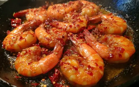 Friterade räkor i en stekpanna med chili och vitlök. De ser saftiga och smakrika ut.
