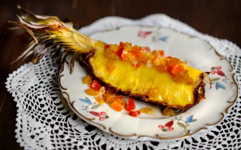 En saftig ananasskiva, toppad med kanderad frukt, serverad på en vacker tallrik. Ett konstverk som visar hur man kan dela ananas utan kniv.