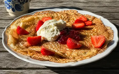 En stor pannkaka med vispad grädde, jordgubbar och sylt. Perfekt för ett enkelt pannkakor recept.