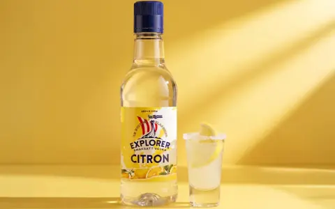 En flaska Explorer Citron vodka bredvid ett glas med en lemon drops shot, garnerad med citronskiva och saltkant.