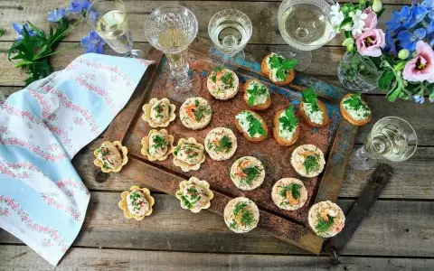 Små, läckra snacks till bubbel, serverade på ett fat med blommor och glas. Perfekt för en festlig stund.