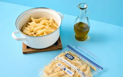 Koka pasta och förbered för att frysa in den. En kastrull med penne, en flaska olivolja och en fryspåse syns.