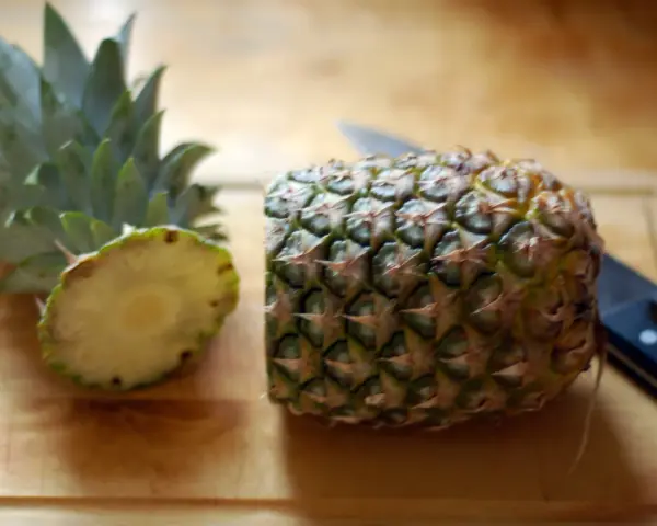 En ananas är delad på mitten på en skärbräda, redo för att visa hur skalar man en ananas. En kniv ligger bredvid.