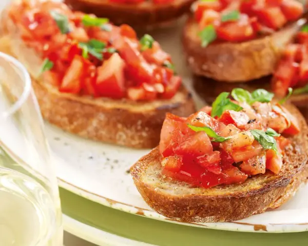 Krispiga bruschettor med färska tomater och basilika, perfekt för ett italienskt recept. Ett glas vitt vin till.