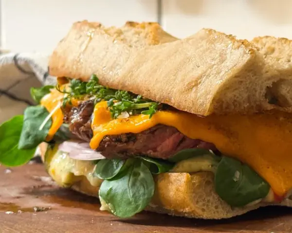 En saftig steak sandwich med smält ost, färska gröna blad och krispigt bröd.