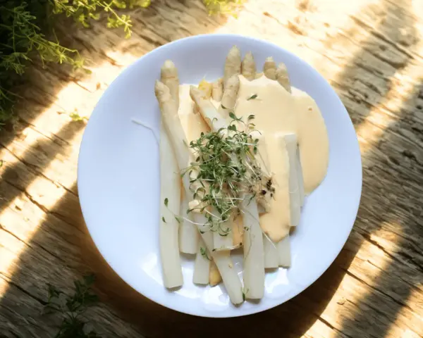 Vit sparris serverad med en krämig sås och toppad med färska groddar. En delikatess som smakar sommar.