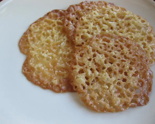 Tre gyllene, tunna havreflarn med ett vackert nätmönster ligger på en vit tallrik. Perfekt för ett enkelt havreflarn recept.