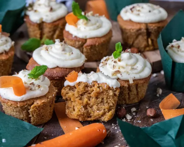 Fluffiga morotskaka muffins med krämig frosting, toppade med nötter och en liten morotsdekoration. Perfekta för fikat!