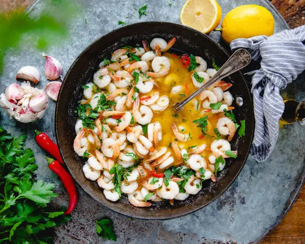 En panna med saftiga räkor i en gyllene sås, perfekt för ett snabbt gambas recept. Garnerad med färsk persilja, chili och vitlök.