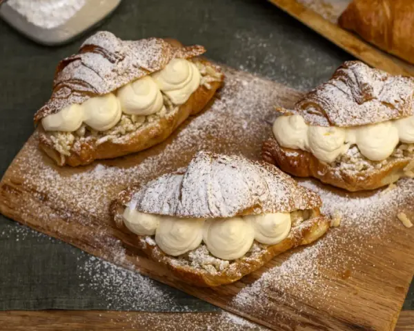Tre semlor fyllda med grädde och mandelmassa, pudrade med florsocker på en träbricka.