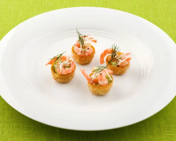 Fyra små, krispiga tempura rolls med räkor och dill på en vit tallrik.