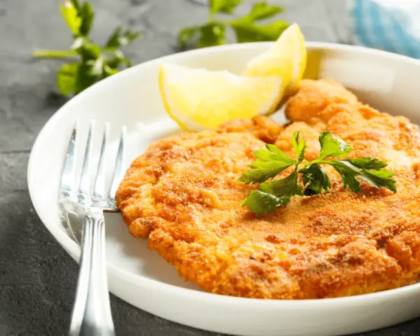 En gyllene schnitzel med citron och persilja, perfekt till ett glas vin.