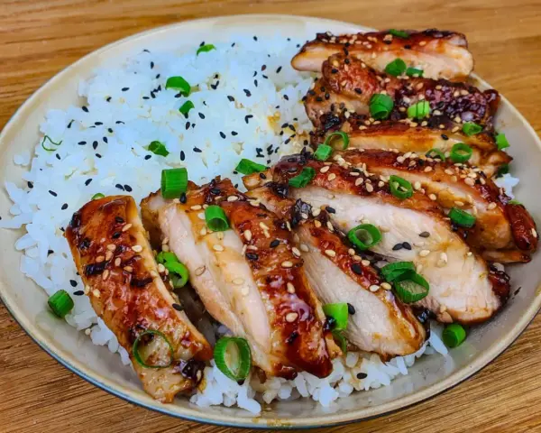 Skivad kyckling i gochujang marinad, serverad med ris och toppad med sesamfrön och salladslök. En härlig rätt som lockar smaklökarna.