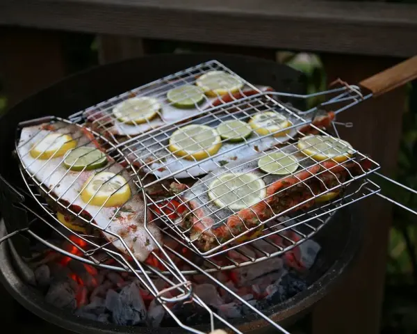 Grillad fisk med citron- och limeskivor på en kolgrill. Doften av sommar och god mat sprider sig.