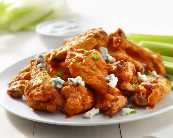 En tallrik med saftiga buffalo wings, toppade med blåmögelost och gräslök, serveras med selleristavar och en skål med dippsås.