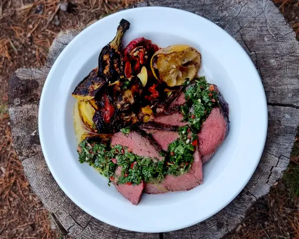 Skivat picanha på en tallrik med grillade grönsaker och citron. Perfekt för en somrig picanha grilla.
