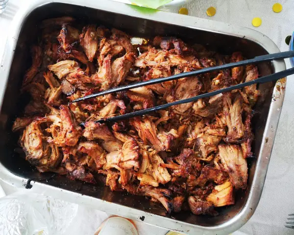 Saftigt, dras isär fläskkött i en ugnsform, redo att serveras. Ett perfekt carnitas recept för en festmåltid.