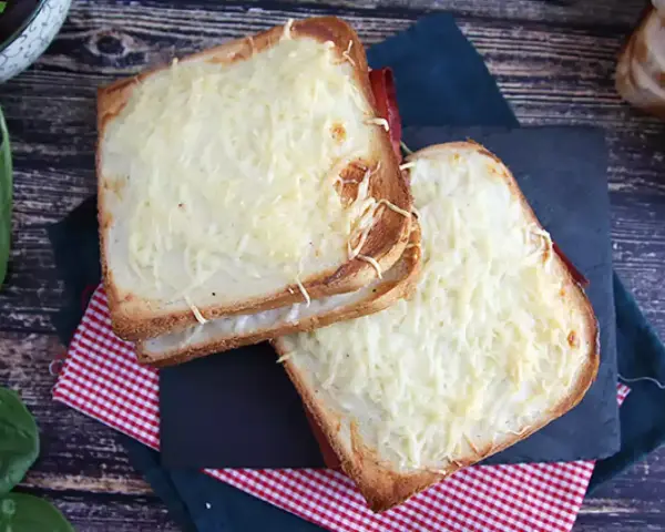 Två gyllene croque monsieur-smörgåsar med smält ost och skinka, serverade på en rutig duk.