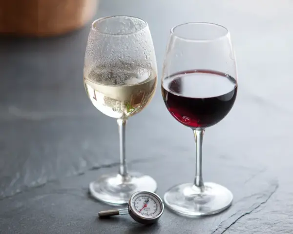 Två glas vin, ett vitt och ett rött, med en termometer bredvid. Perfekt vitt vin temperatur är viktigt för njutning.
