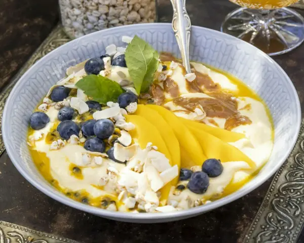 En skål med yoghurt, blåbär, passionsfrukt och vackert skivad mango. Toppad med kokoschips och puffat spannmål.