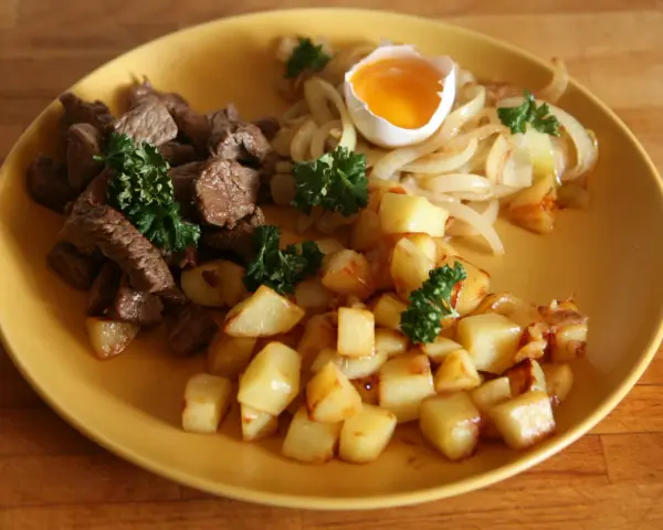 En tallrik med stekt kött, stekt potatis, stekt lök och ett kokt ägg. Ett klassiskt husmanskost recept som passar perfekt för en vardagsmiddag.