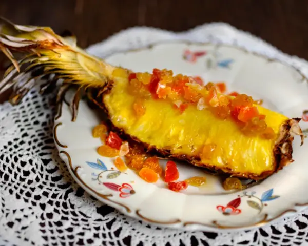 En saftig ananasskiva, toppad med kanderad frukt, serverad på en vacker tallrik. Ett konstverk som visar hur man kan dela ananas utan kniv.