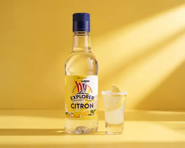 En flaska Explorer Citron vodka bredvid ett glas med en lemon drops shot, garnerad med citronskiva och saltkant.