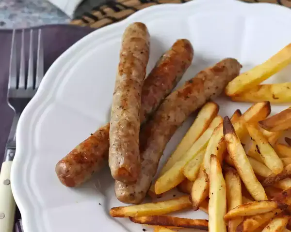 Saftig korv i airfryer med krispiga pommes frites på en vit tallrik. Enkel och god middag.
