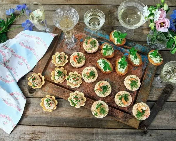 Små, läckra snacks till bubbel, serverade på ett fat med blommor och glas. Perfekt för en festlig stund.