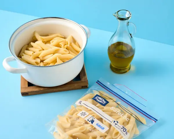 Koka pasta och förbered för att frysa in den. En kastrull med penne, en flaska olivolja och en fryspåse syns.