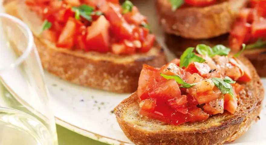 Krispiga bruschettor med färska tomater och basilika, perfekt för ett italienskt recept. Ett glas vitt vin till.