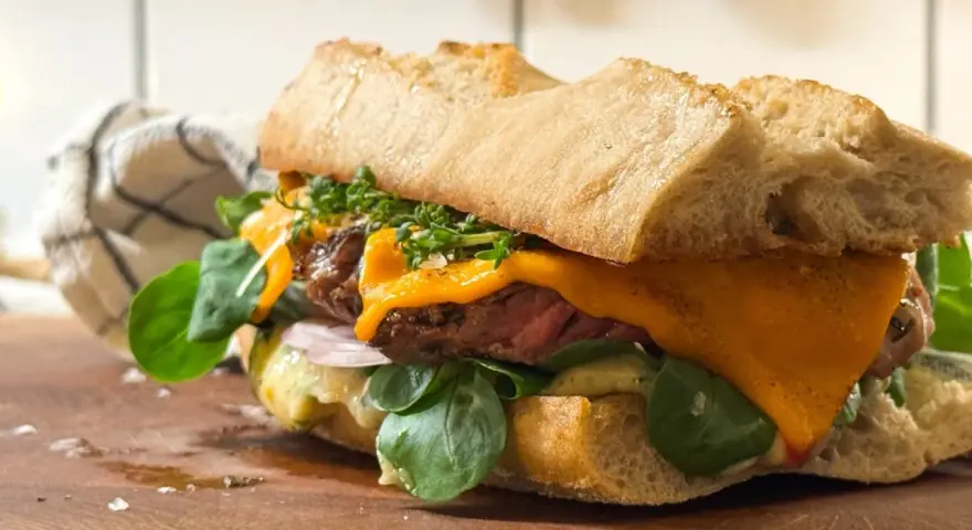 En saftig steak sandwich med smält ost, färska gröna blad och krispigt bröd.