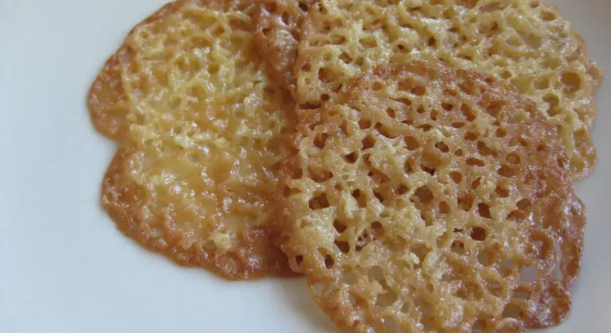 Tre gyllene, tunna havreflarn med ett vackert nätmönster ligger på en vit tallrik. Perfekt för ett enkelt havreflarn recept.