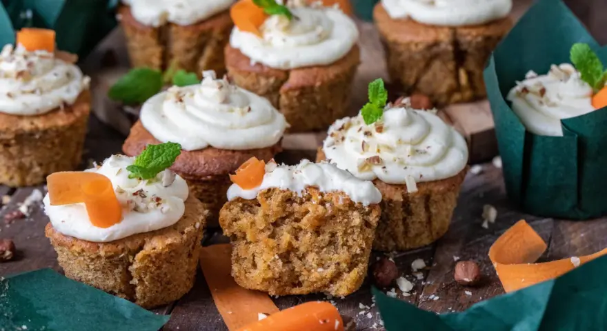 Fluffiga morotskaka muffins med krämig frosting, toppade med nötter och en liten morotsdekoration. Perfekta för fikat!