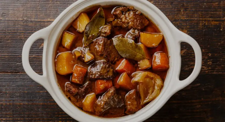 En vit gryta fylld med mustig boeuf bourguignon, med möra köttbitar, potatis och morötter. Perfekt vin till boeuf bourguignon.