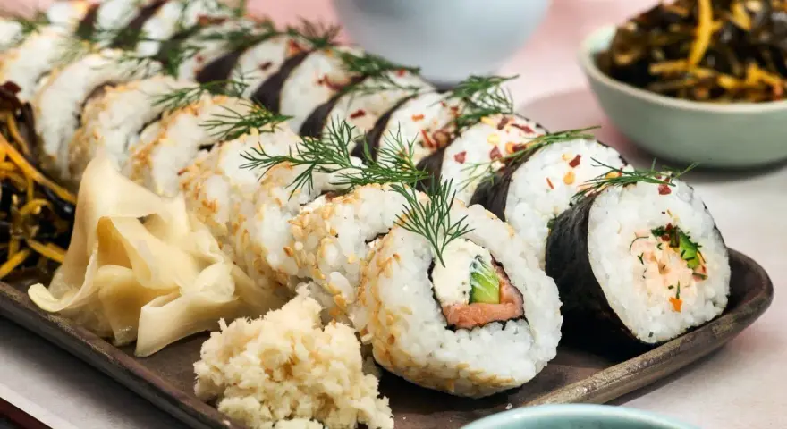 Välsmakande hemmagjord sushi med lax, gurka och krämig fyllning, garnerad med dill och sesamfrön. Serveras med ingefära och wasabi.