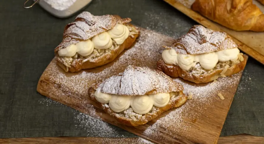Tre semlor fyllda med grädde och mandelmassa, pudrade med florsocker på en träbricka.