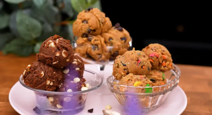Tre skålar med härlig cookie dough paj: en med choklad och vita chokladknappar, en med chokladknappar och en med färgglada godisbitar.