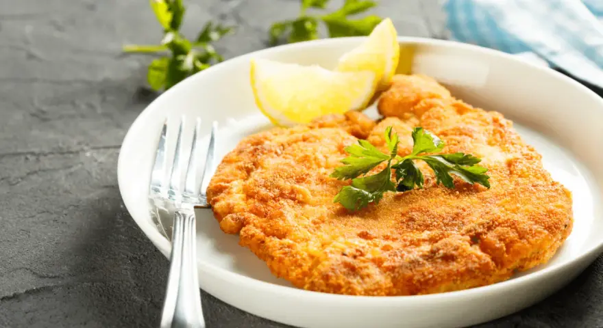 En gyllene schnitzel med citron och persilja, perfekt till ett glas vin.