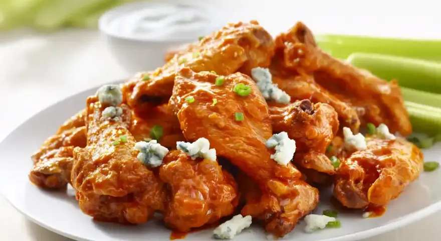 En tallrik med saftiga buffalo wings, toppade med blåmögelost och gräslök, serveras med selleristavar och en skål med dippsås.