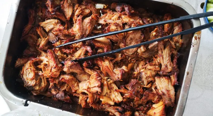 Saftigt, dras isär fläskkött i en ugnsform, redo att serveras. Ett perfekt carnitas recept för en festmåltid.