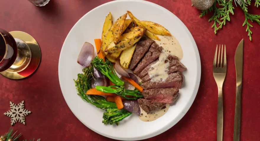 En festlig tallrik med saftig biff, rostade potatisklyftor, grönsaker och en krämig sås. Perfekt glutenfri mat för högtider.