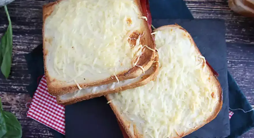 Två gyllene croque monsieur-smörgåsar med smält ost och skinka, serverade på en rutig duk.