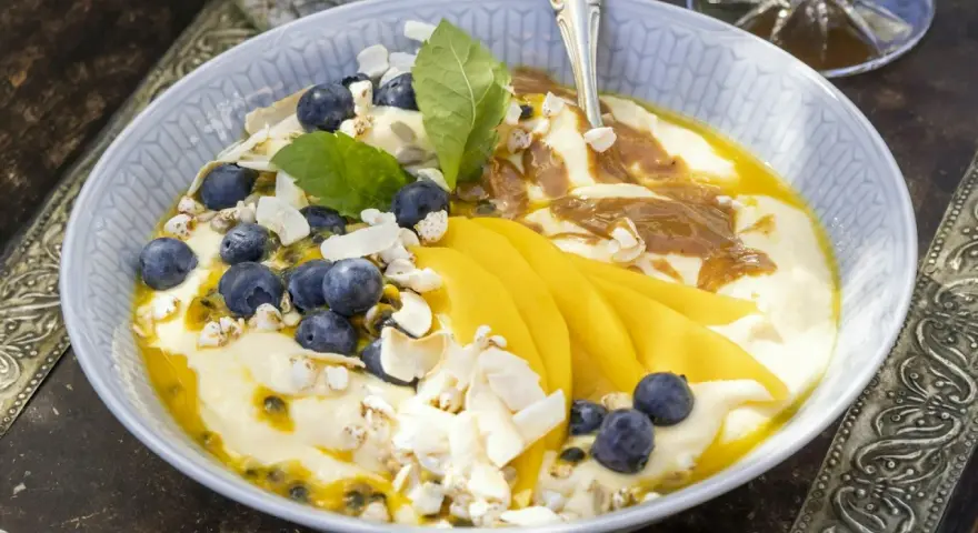 En skål med yoghurt, blåbär, passionsfrukt och vackert skivad mango. Toppad med kokoschips och puffat spannmål.