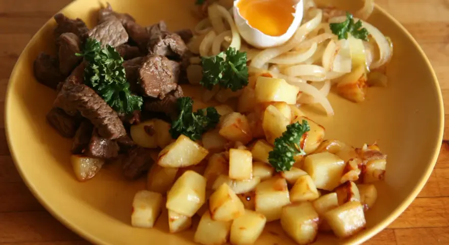 En tallrik med stekt kött, stekt potatis, stekt lök och ett kokt ägg. Ett klassiskt husmanskost recept som passar perfekt för en vardagsmiddag.