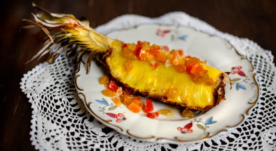 En saftig ananasskiva, toppad med kanderad frukt, serverad på en vacker tallrik. Ett konstverk som visar hur man kan dela ananas utan kniv.